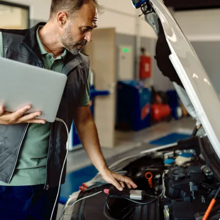 auto e_0001_auto-repairman-using-laptop-while-examining-car-engine-workshop