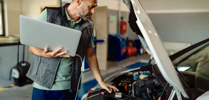 auto e_0001_auto-repairman-using-laptop-while-examining-car-engine-workshop